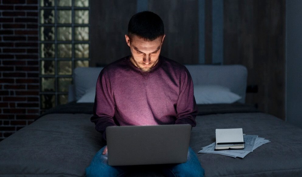 A young man sitting in bed with a laptop | TechReviewGarden